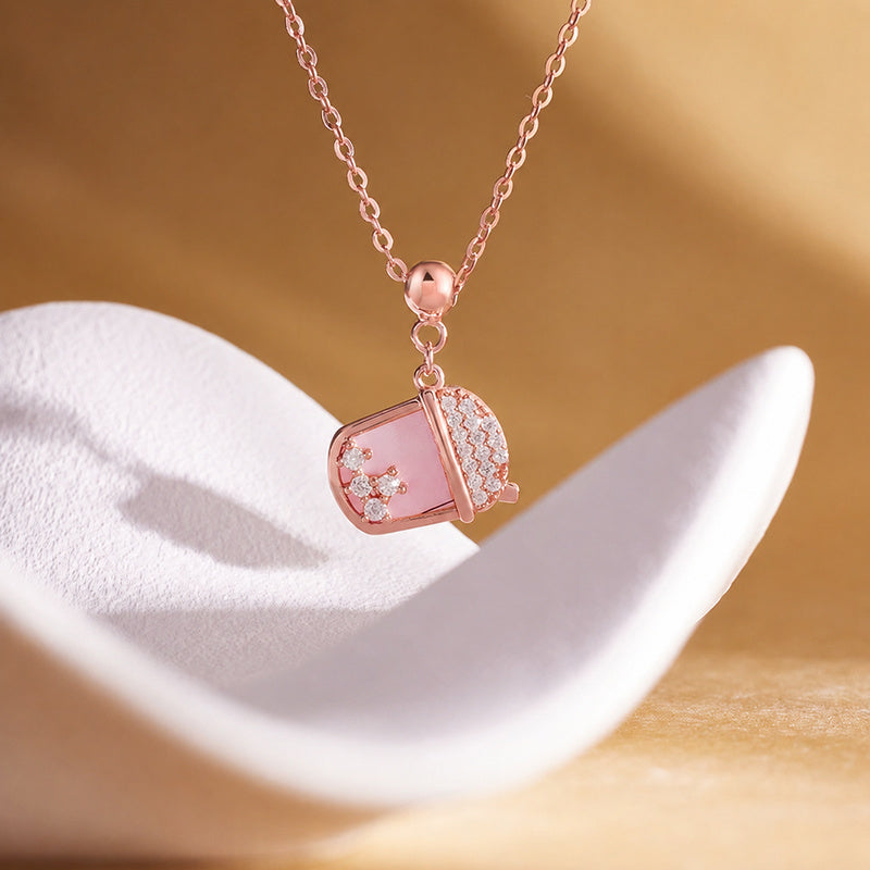 Pink mother-of-pearl milk tea cup necklace on a warm sculptural display