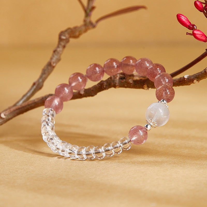 Clear quartz and red strawberry crystal bracelet displayed against a flowering branch