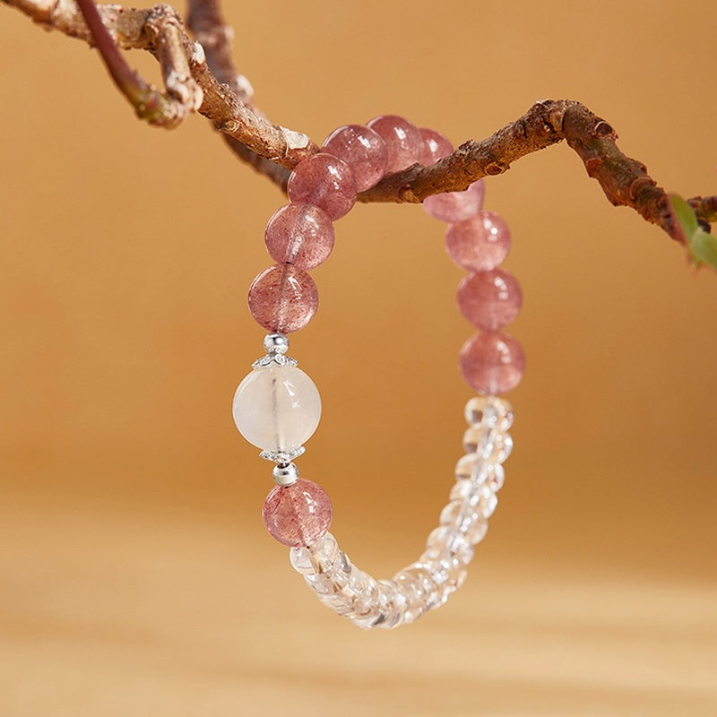 Strawberry crystal bracelet hanging from a branch with clear quartz beads visible