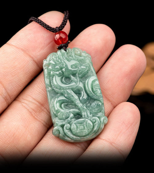 Single green jade dragon pendant held in a palm with dark cord, showing its scale and carved detail