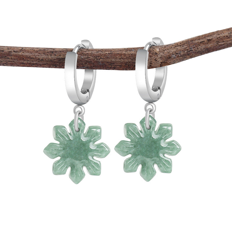 Green jade sunflower earrings hanging from silver hoops on a wooden branch