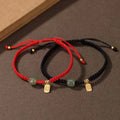 Red and black couple cord bracelets with green jade bead and gold-plated Fu charms displayed together.