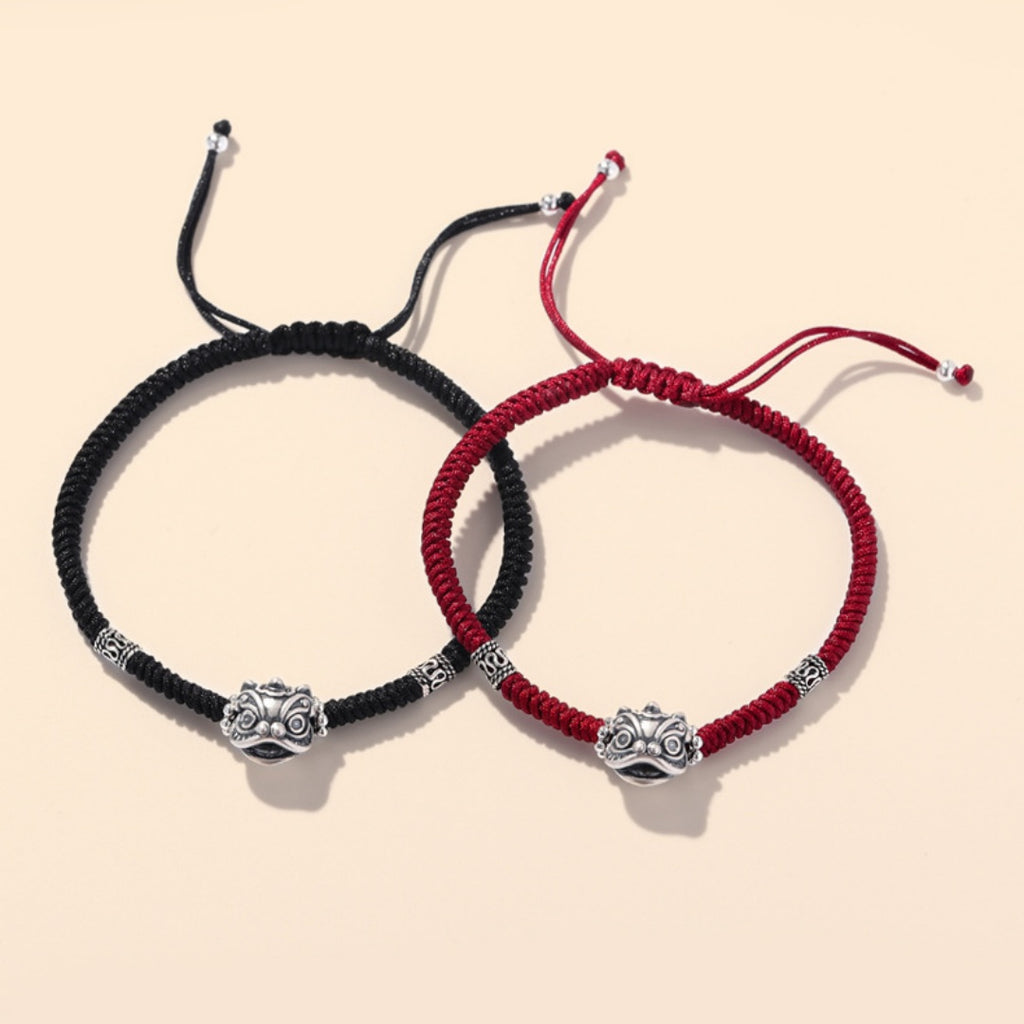 Matching red and black braided bracelets displayed together with oxidized silver guardian face charms.