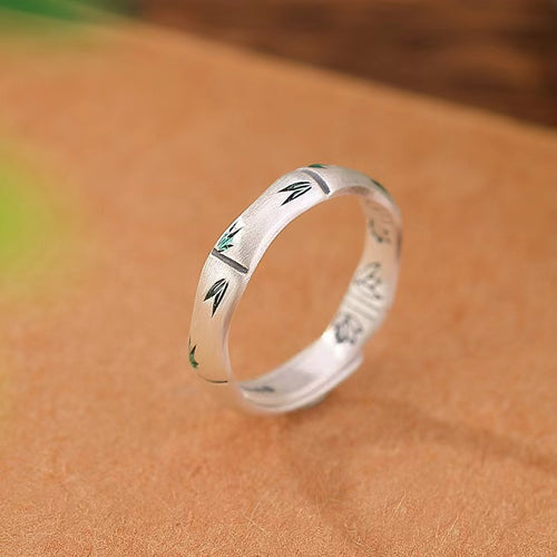 Silver bamboo ring standing on a warm brown surface with green enamel leaf details.