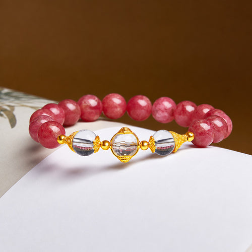 Clear quartz Wealth Deity and pink rhodonite bracelet on a warm brown and paper background