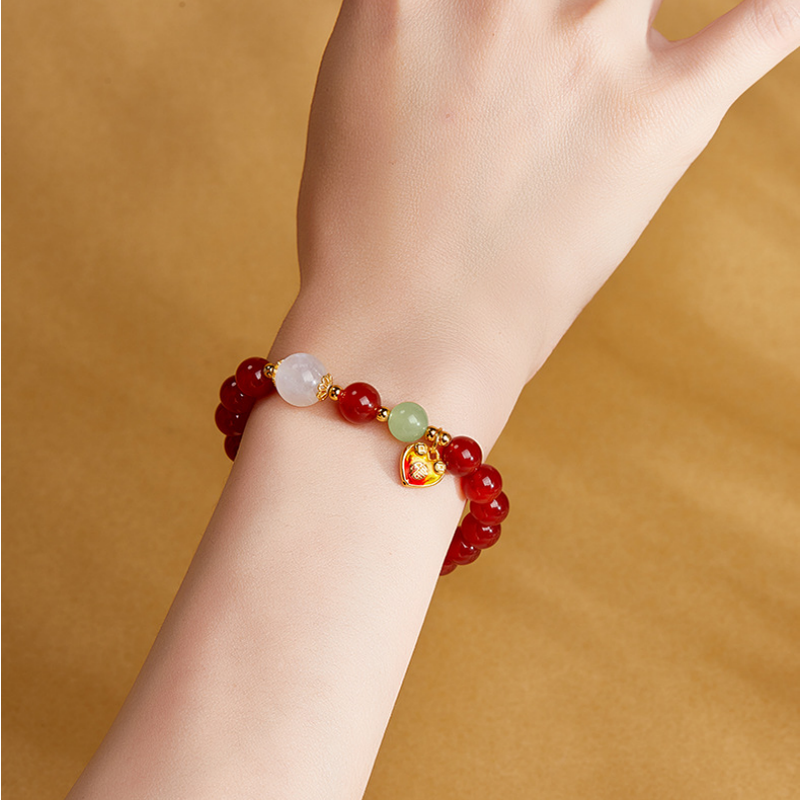 Red agate heart bracelet worn on a wrist against a warm golden background