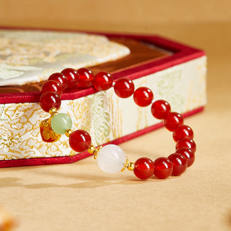 Red agate bracelet with pale jade and moonstone beside a brocade box