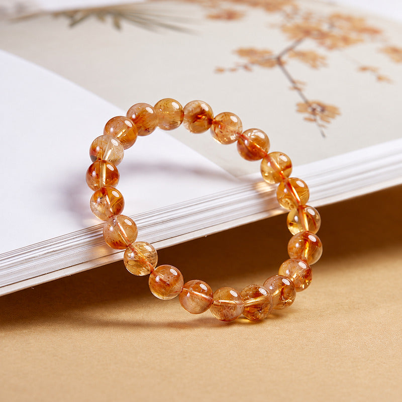 Yellow phantom quartz bracelet leaning against a book in warm light