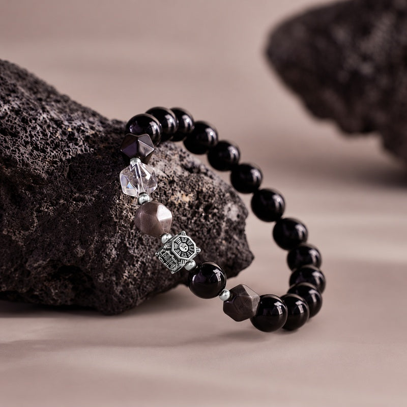 Obsidian bracelet draped over textured rock with engraved Bagua detail