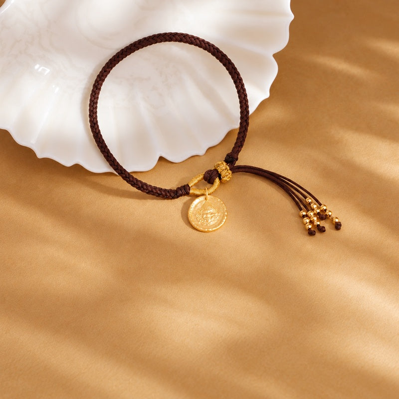 Yellow Wealth Deity woven bracelet on golden fabric beside a shell