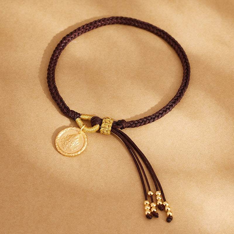 Brown braided bracelet and gold-tone deity charm on fabric
