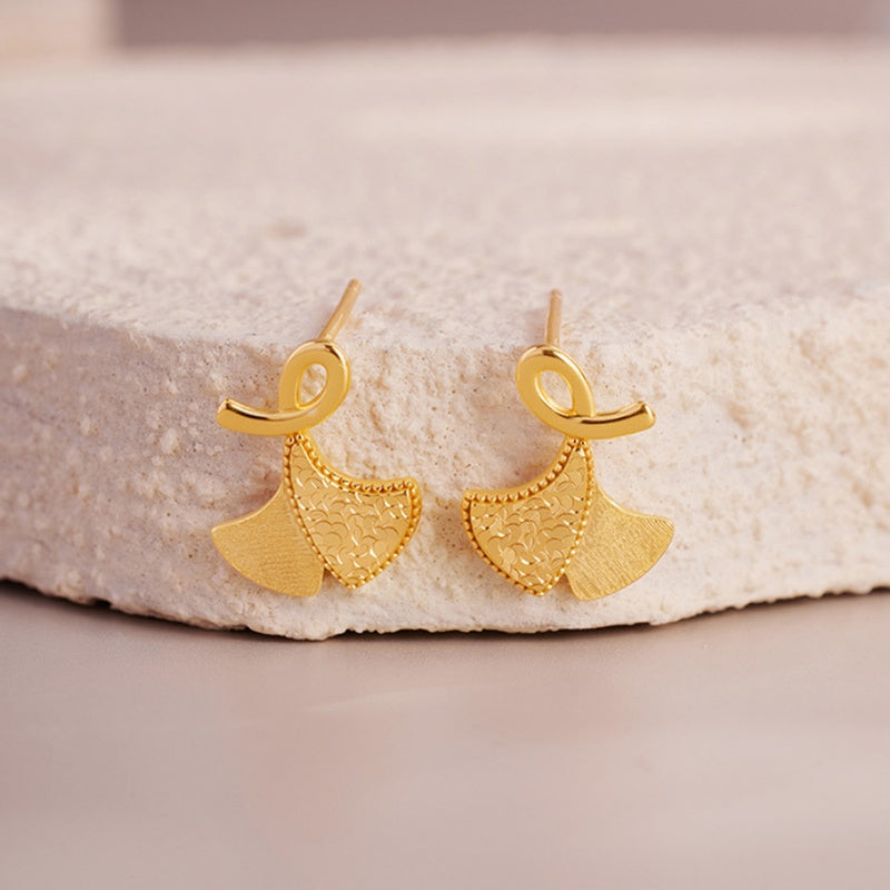 Pair of gold-tone 925 silver ginkgo leaf stud earrings against a pale stone