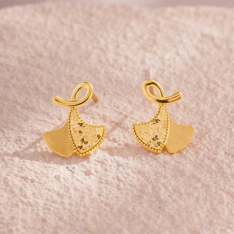 Textured and polished ginkgo leaf earrings on a pale textured background