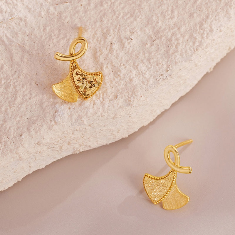 Angled view of the ginkgo leaf earring pair beside a pale stone