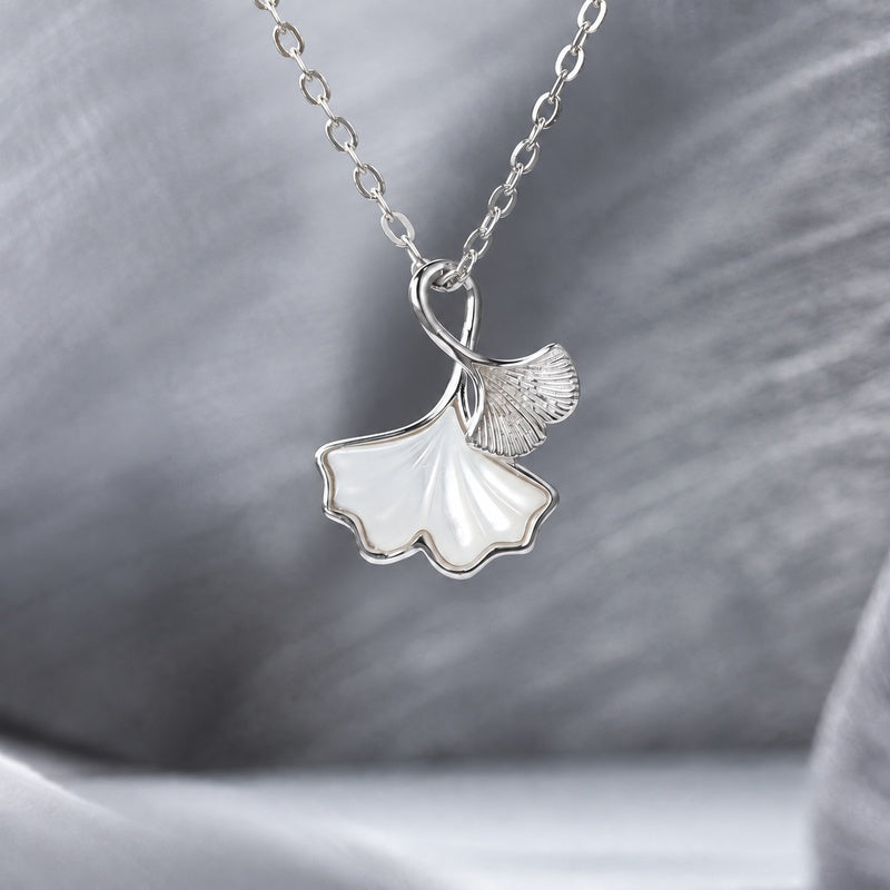 White mother-of-pearl and silver ginkgo leaf necklace suspended against soft gray fabric