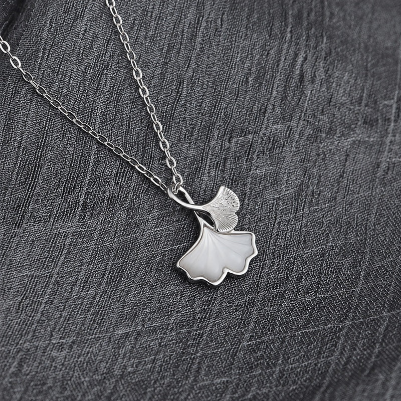 Silver and white ginkgo leaf necklace resting on woven gray fabric