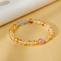 Yellow tower quartz bracelet with strawberry crystal focal bead and three gray moonstone beads on a warm golden background