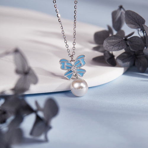 Blue enamel bow and imitation pearl necklace against a blue background with dark foliage