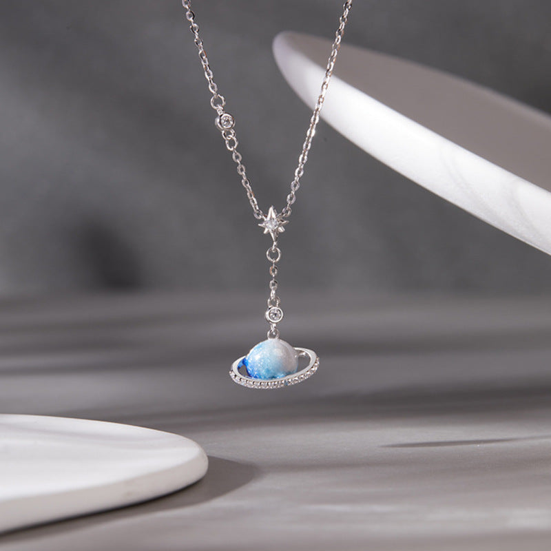 Blue enamel ringed planet necklace suspended against a gray background