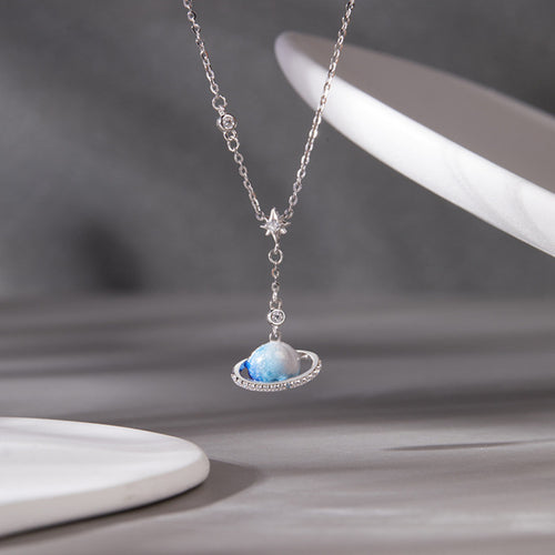 Blue enamel ringed planet necklace suspended against a gray background
