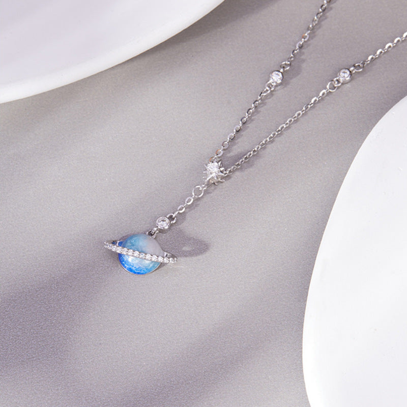 Blue enamel planet necklace resting on a gray display