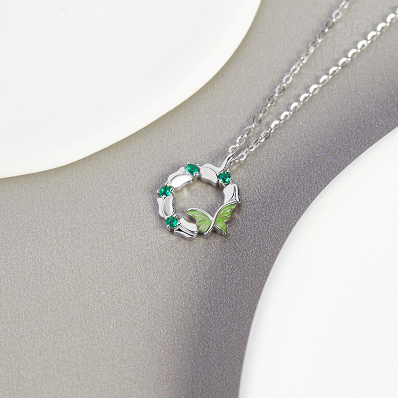 Butterfly wreath necklace resting on a textured silver surface