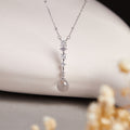 Clear quartz silver drop necklace against cream ceramic and floral background