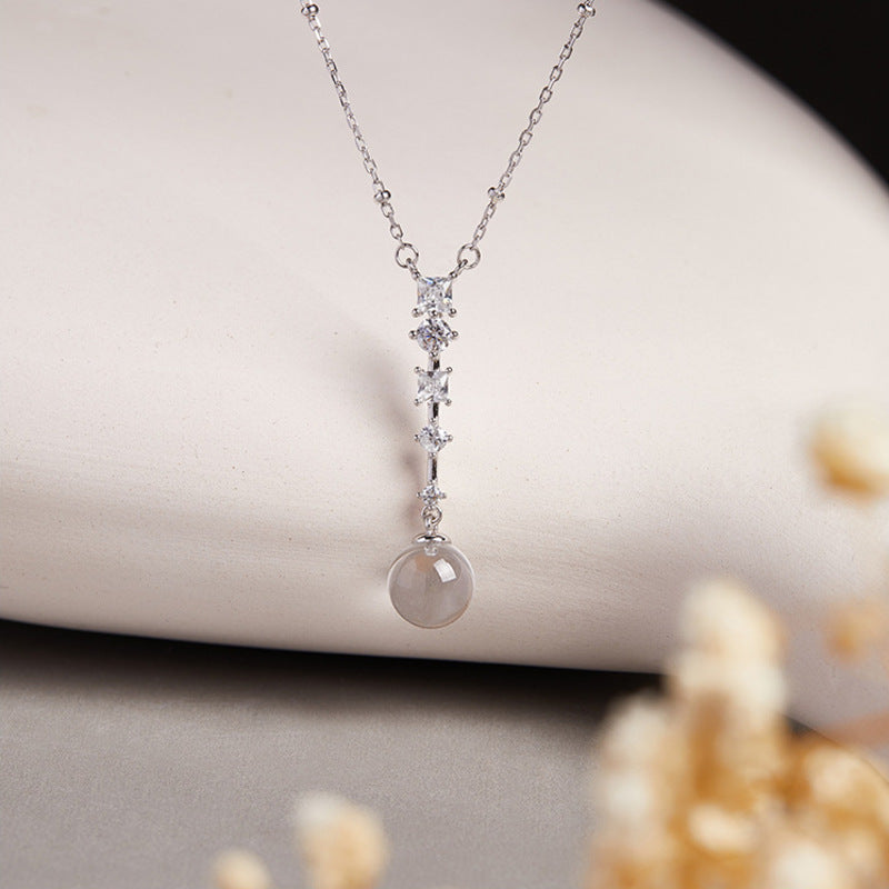 Clear quartz silver drop necklace against cream ceramic and floral background