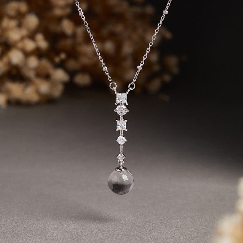 Clear quartz and cubic zirconia pendant suspended against a dark floral background