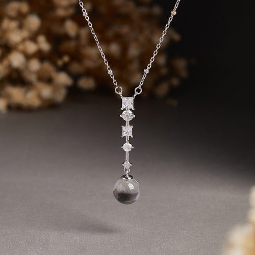 Clear quartz and cubic zirconia pendant suspended against a dark floral background