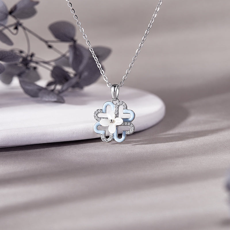 Blue enamel clover necklace with a white mother-of-pearl flower on a grey fabric background