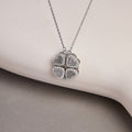 Silver magnetic heart clover necklace resting against a pale curved backdrop