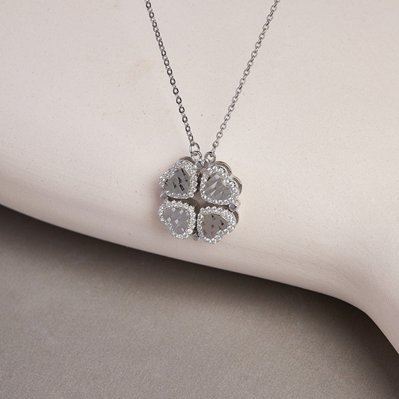 Silver magnetic heart clover necklace resting against a pale curved backdrop