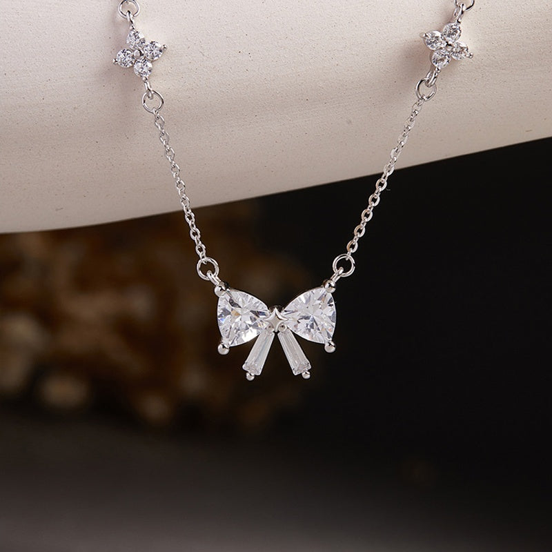 Silver bow and clover necklace suspended against a dark background