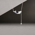 Mother-of-pearl whale necklace with blue enamel tail and synthetic pearl drop on a gray background