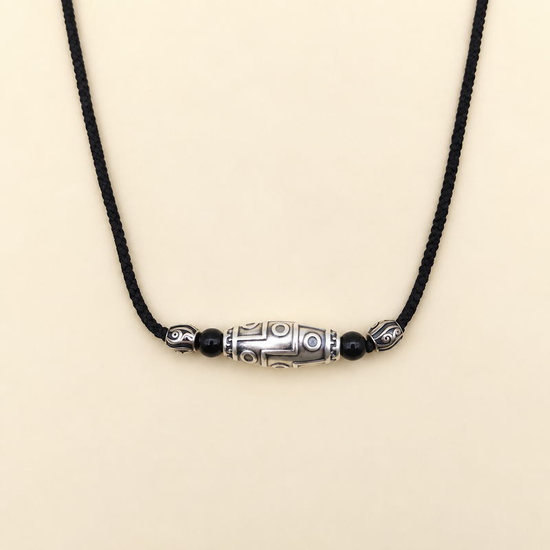 Nine-eye silver Dzi necklace on a warm cream background