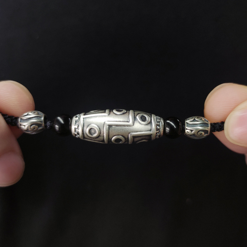 Hand-held close-up of the nine-eye silver Dzi pendant