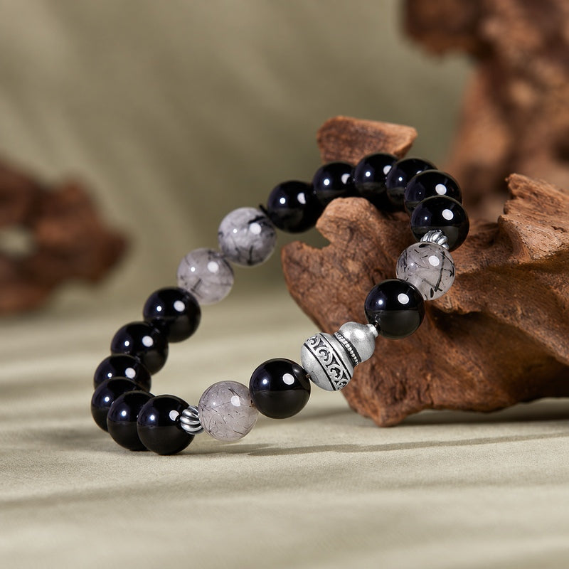 Gourd obsidian and black inclusion quartz bracelet resting on natural wood