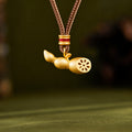 Gold-colored lotus-root pendant hanging from a braided cord against an olive background