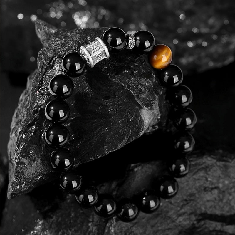 Obsidian mantra bracelet draped over dark rock
