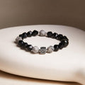 Map stone and obsidian Bagua bracelet resting on a cream cushion with a taupe background