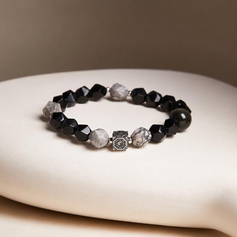 Map stone and obsidian Bagua bracelet resting on a cream cushion with a taupe background