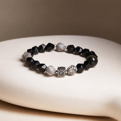 Map stone and obsidian Bagua bracelet resting on a cream cushion with a taupe background