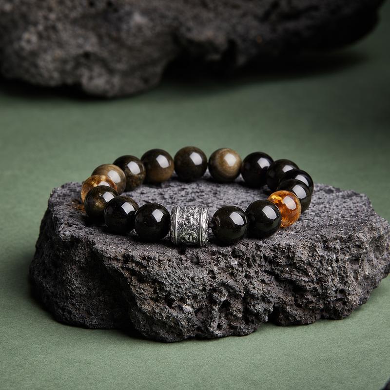 Gold sheen obsidian and black obsidian bracelet resting on a dark rock with a green background