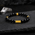 Black obsidian blessing bracelet with engraved gold bar on dark slate
