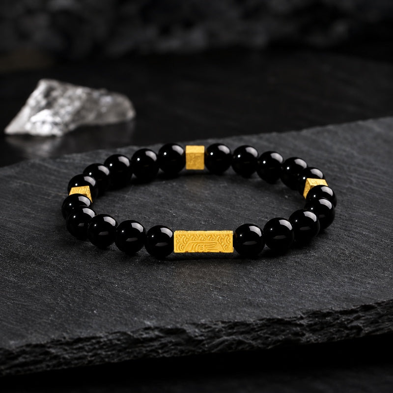 Black obsidian blessing bracelet with engraved gold bar on dark slate
