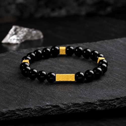 Black obsidian blessing bracelet with engraved gold bar on dark slate