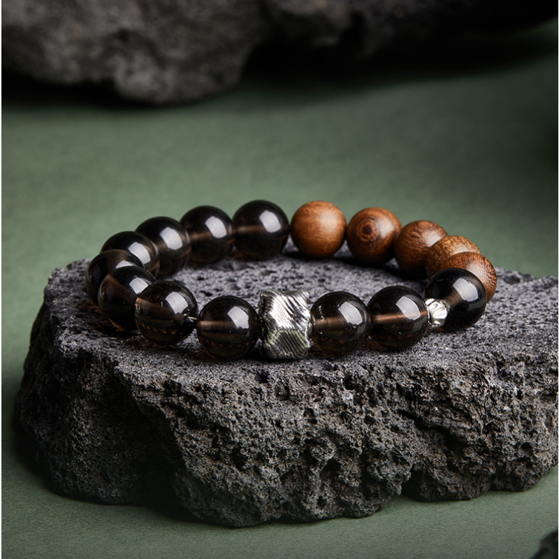 Obsidian and golden silk wood bracelet on a dark stone with a green background