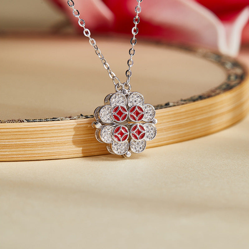 Silver magnetic clover necklace with red enamel coin motifs on a warm floral background