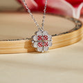 Silver magnetic clover necklace with red enamel coin motifs on a warm floral background